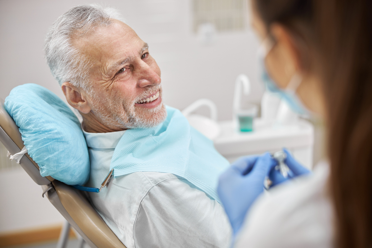 Senior patient of a clinic sitting in a dental chair and watching his dentist start a dental drill