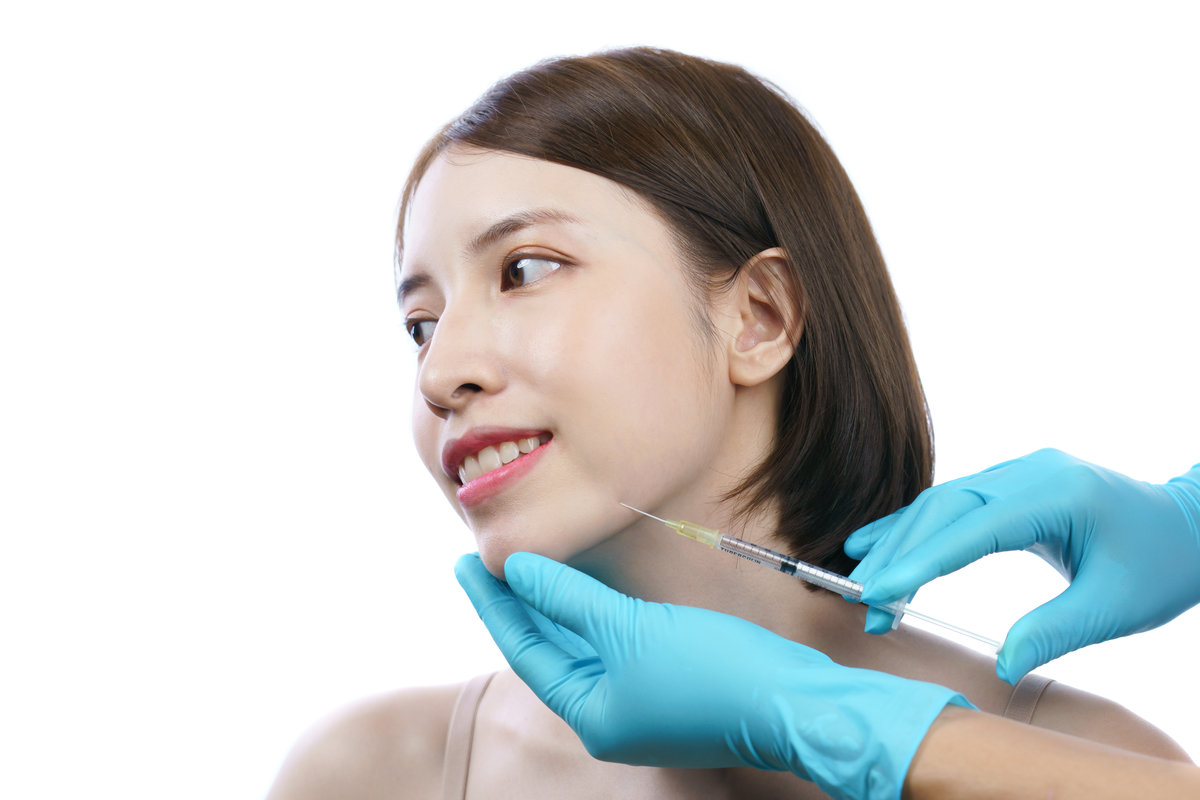 Hands of beautician injecting Botulinum toxin type A to asian woman in jaw area.