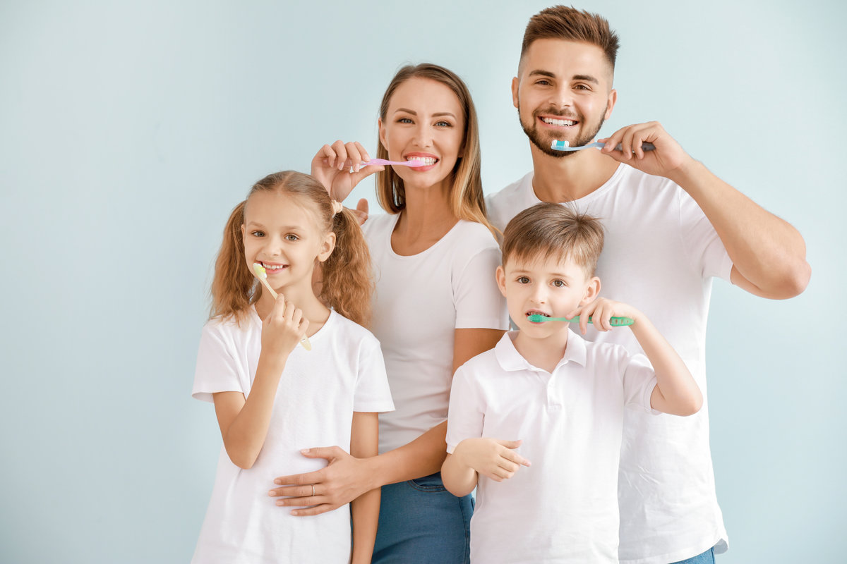 Portrait of family brushing teeth on light background
