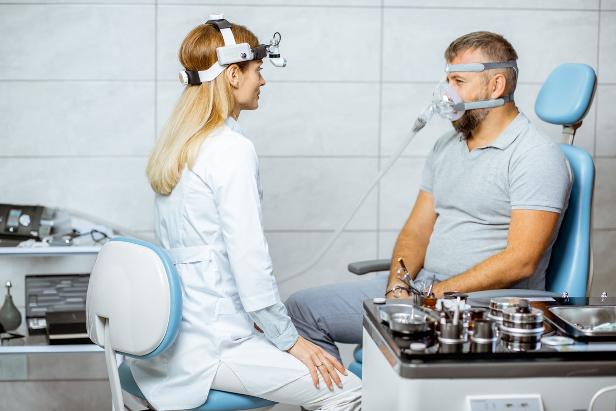 Adult man during a medical breathing treatment with respiratory mask against snoring sitting with doctor