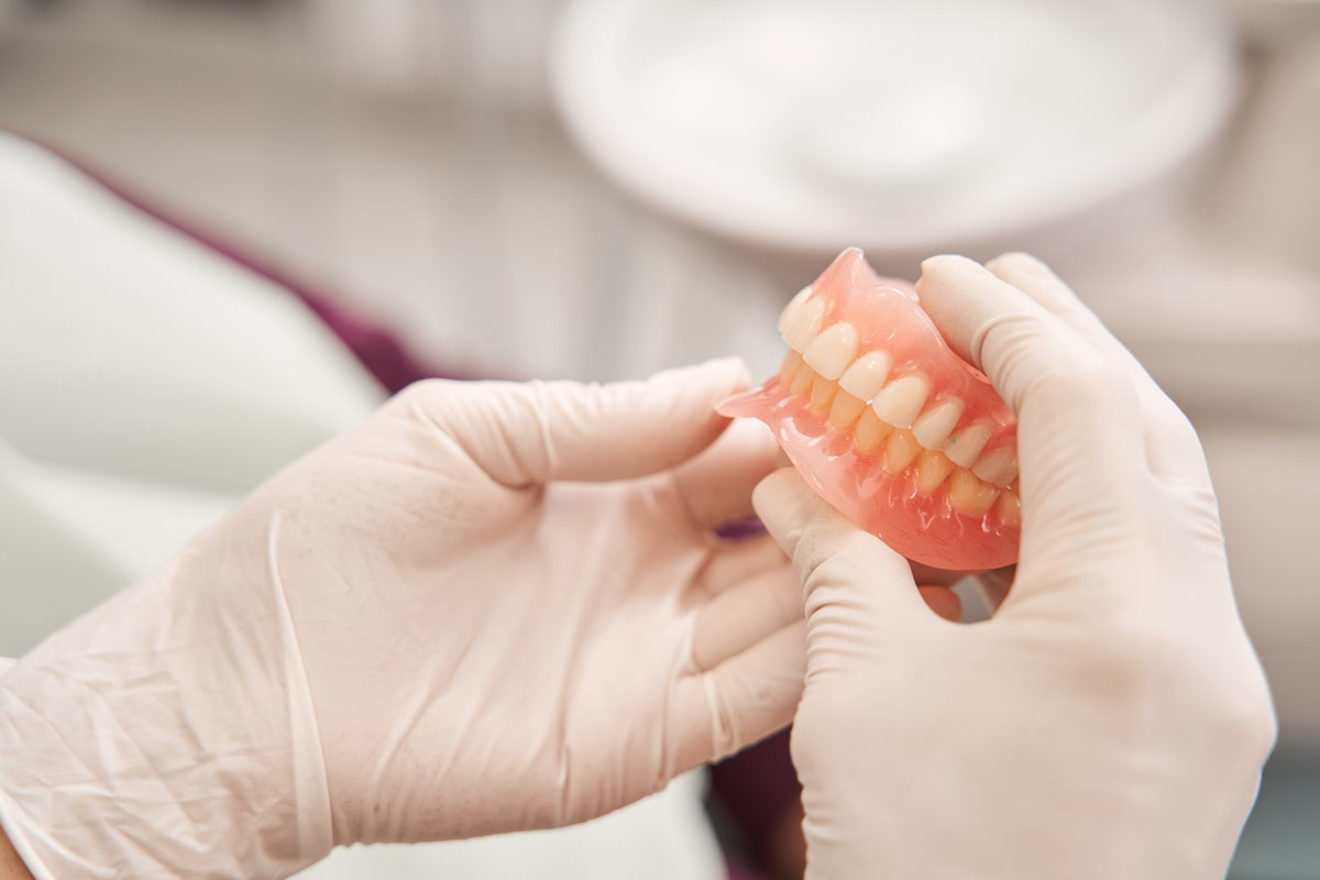 Cropped view of the dentist holding dentures in her hands. Dental prosthesis in the hands of the doctor close-up. Front view of complete denture. Dentistry conceptual photo. Prosthetic dentistry. False teeth