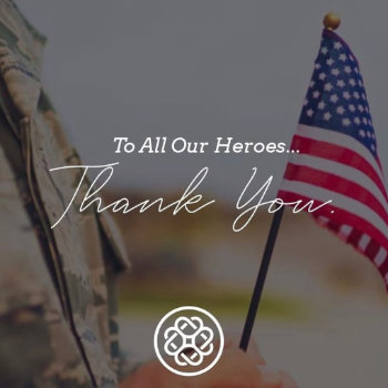 A person in military uniform holds a small American flag. Text over the image reads, "To All Our Heroes... Thank You." A circular logo appears at the bottom.