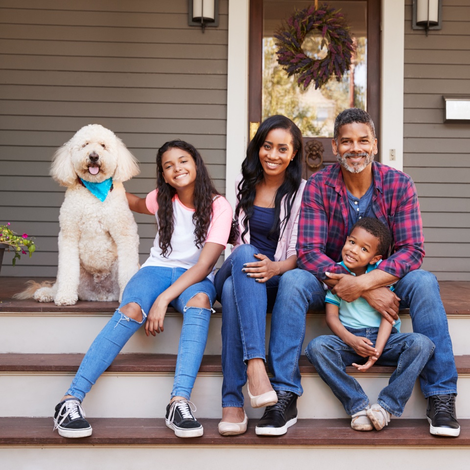 Family With Children And Pet Dog Sit On Steps Of Home