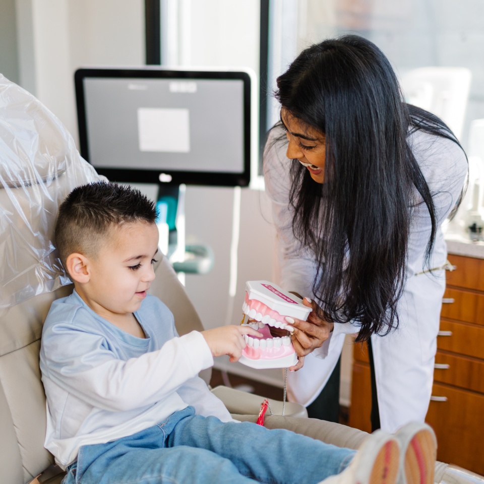 A dentist shows a young boy how to brush teeth using a large dental model and toothbrush in a dental office.