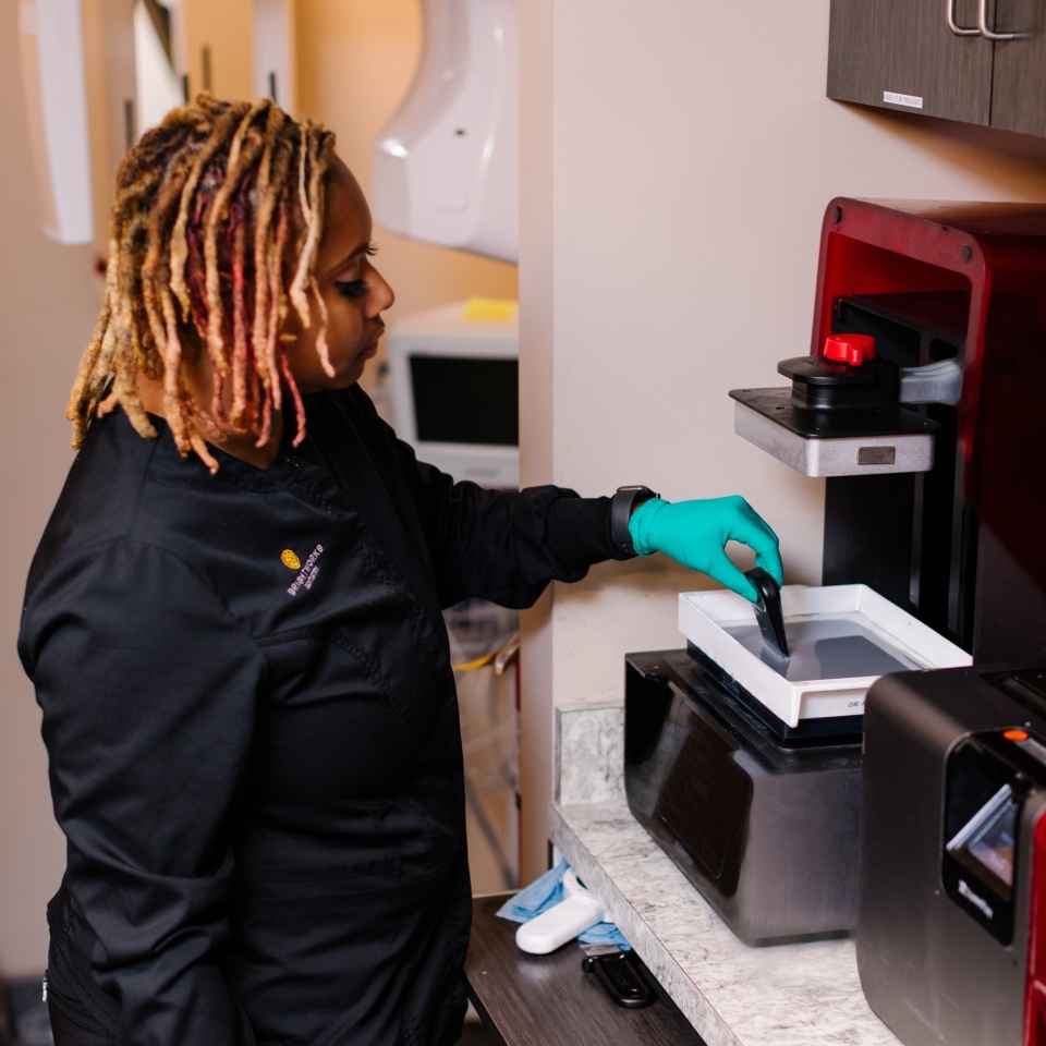 A person wearing gloves and a black uniform operates a piece of laboratory equipment on a countertop in a clinical setting.