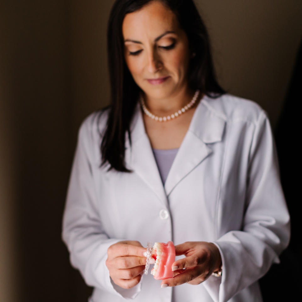 A person in a white lab coat holds a dental model with braces, looking down at it.