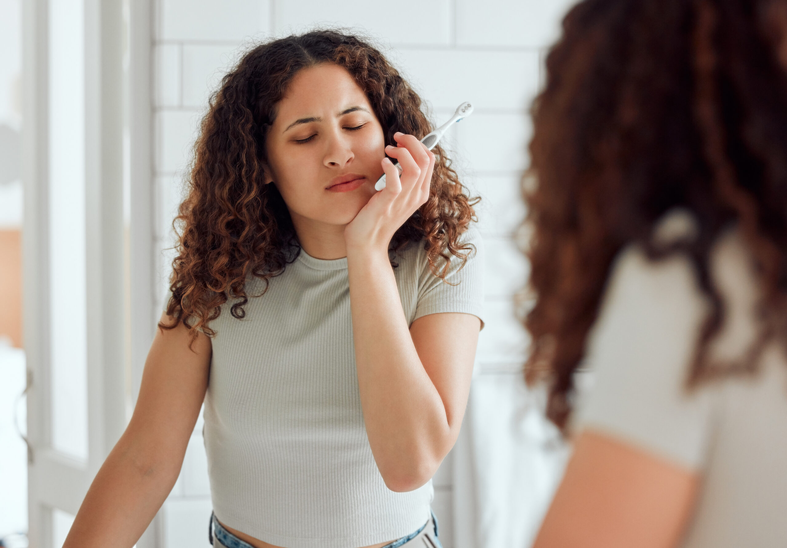 Toothache, oral pain and dental sensitivity for a woman brushing her teeth in the morning. African American female suffering with a painful, hurting or inflammation in her mouth in the bathroom.