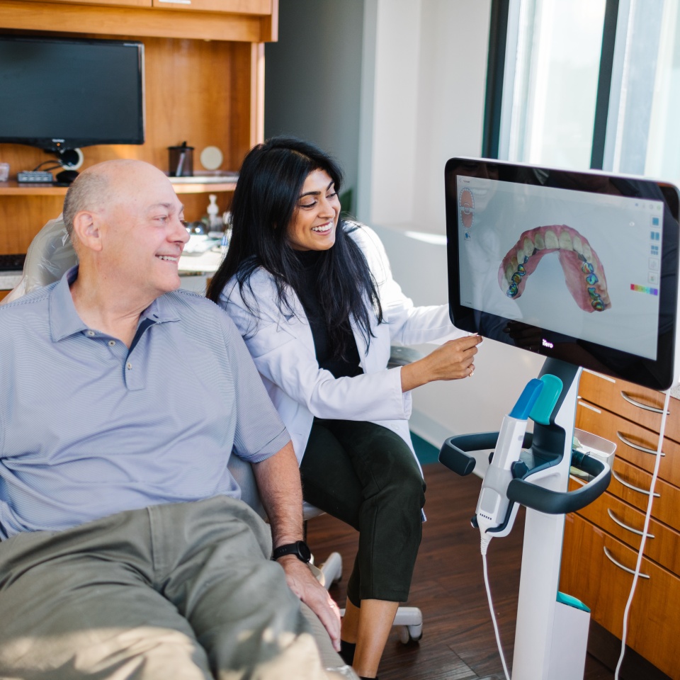 A dentist shows a dental scan on a monitor to a male patient seated in a dental office.