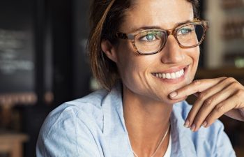 Portrait of beautiful mature woman sitting in cafeteria looking away. Cheerful mature woman wearing eyeglasses thinking with finger on chin. Happy woman relaxing at cafe and smiling.