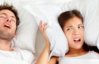 Snoring man. Couple in bed, man snoring and woman can not sleep, covering ears with pillow for snore noise. Young interracial couple, Asian woman, Caucasian man sleeping in bed at home.