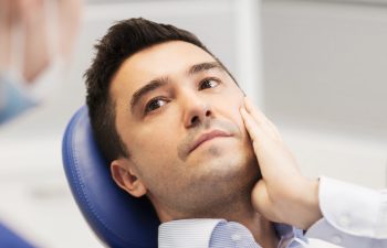 people, medicine, stomatology and health care concept - male patient with toothache complaining to female dentist at dental clinic office