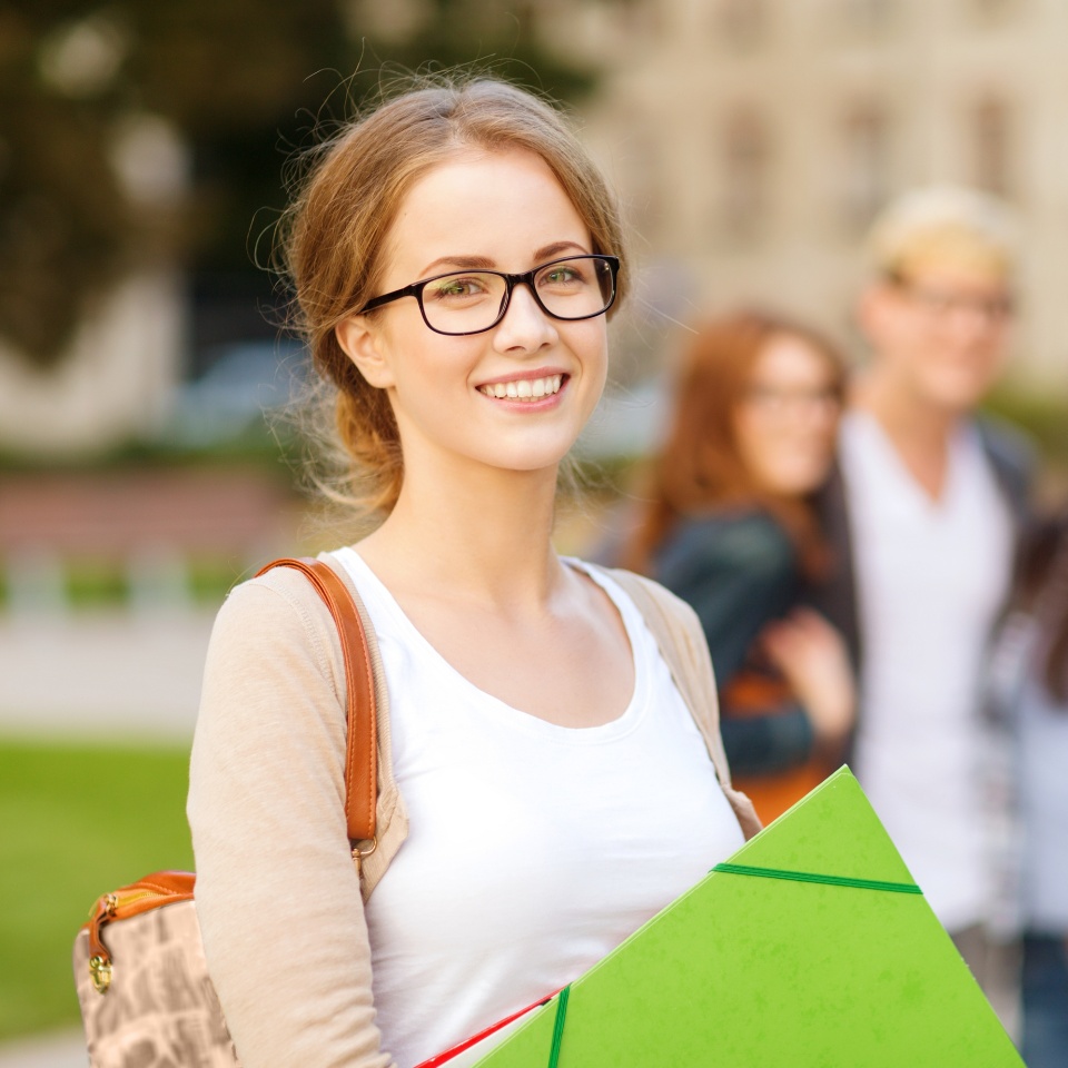 summer holidays, education, campus and teenage concept - smiling female student in black eyeglasses with folders and group in the back
