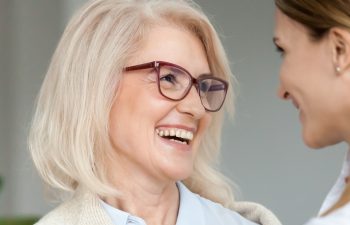 Beautiful aged woman in glasses embracing young adult lady and laughing, smiling attractive senior older mother happy to hug grown-up daughter, warm sincere family bonding having fun together