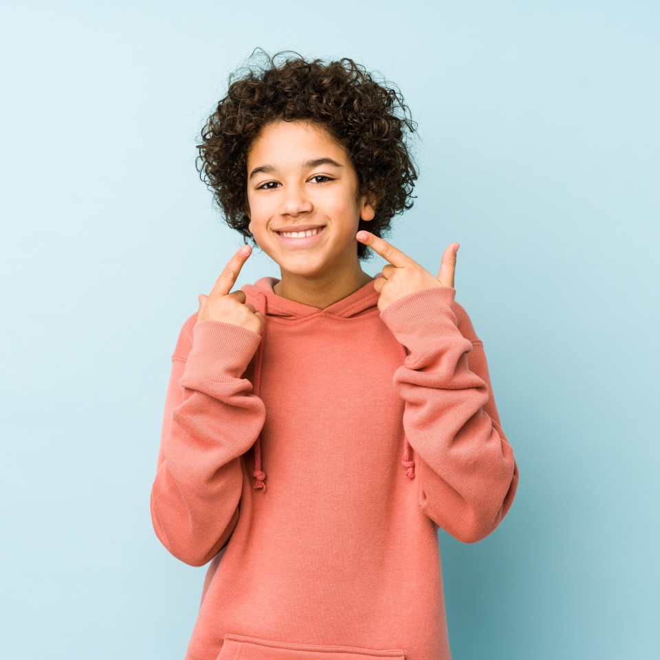 African american little boy isolated smiles, pointing fingers at mouth.