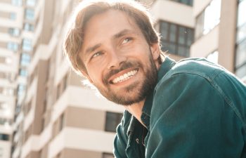 Portrait of handsome smiling stylish hipster lambersexual model.Man dressed in green shirt. Fashion male posing in the street at skyscraper background