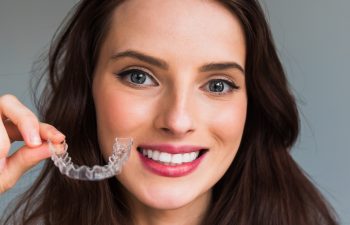 Young beautiful woman holding dental aligner orthodontic to tee