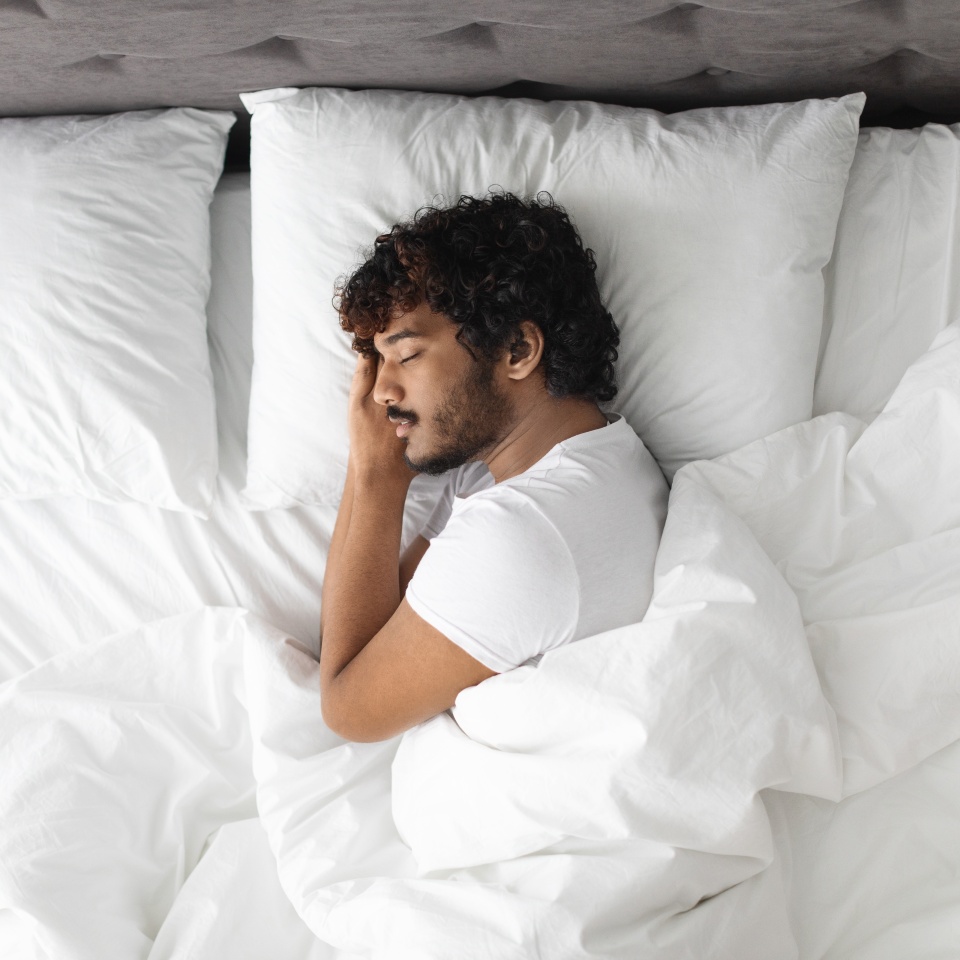 View above of handsome bearded young eastern guy in pajamas resting at home, sleeping on his side with hands under head in comfortable bed., copy space Healthy sleeping concept