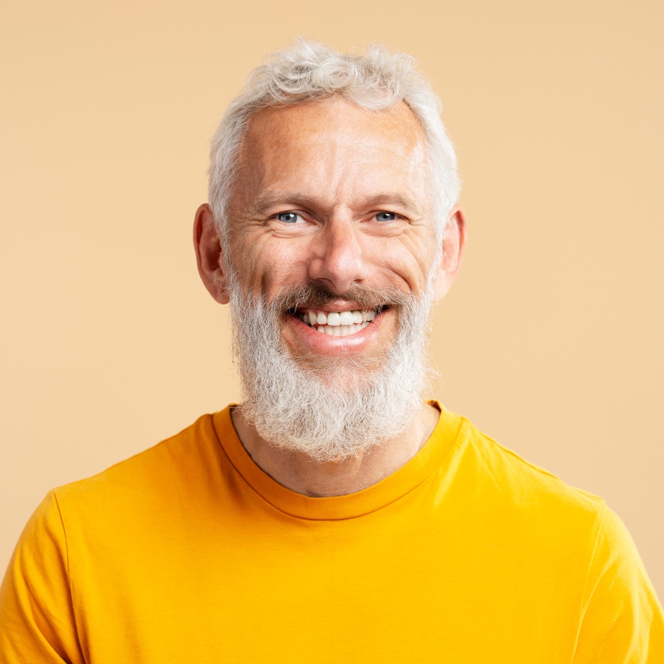 Closeup portrait handsome smiling 50 years old man with stylish gray hair wearing casual orange t shirt, looking at camera isolated on background. Health care, dental treatment concept