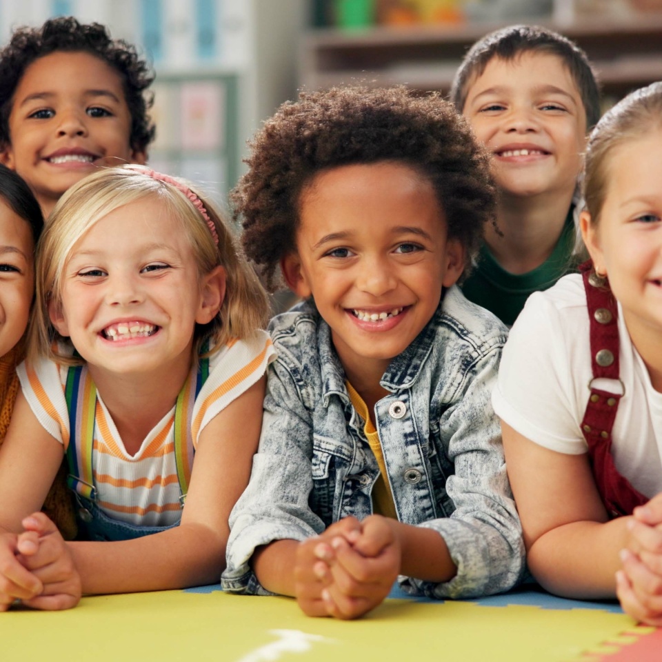 Kindergarten, kids and face with smile on floor for education, knowledge and learning at academy. Students, friends and happy with diversity in school for child development, scholarship and bonding