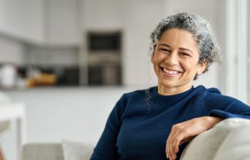 Happy middle aged woman sitting on comfy sofa in living room at home laughing. Smiling mature older lady relaxing on couch looking at camera on couch in modern cozy house. Portrait.