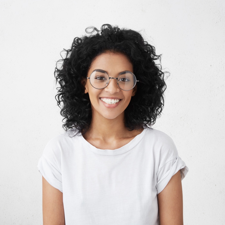 Indoor portrait of beautiful brunette young dark-skinned woman with shaggy hairstyle smiling cheerfully, showing her white teeth to camera while feeling happy and carefree on her first day-off