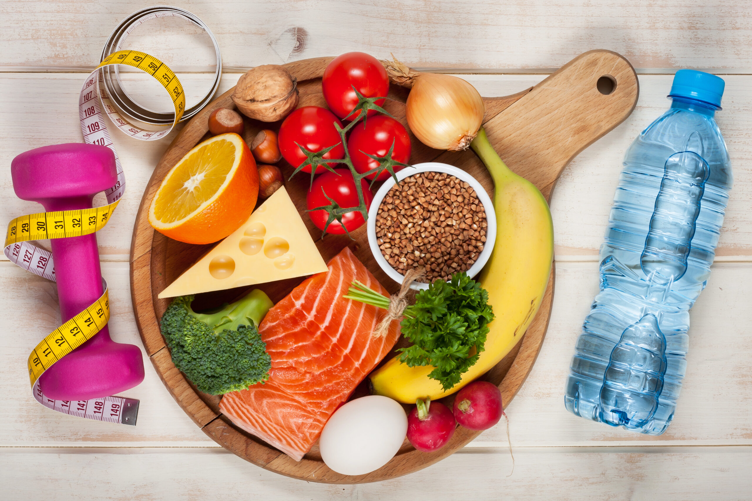 Healthy lifestyle concept. Dumbbell, bottle of water and healthy organic food on wooden table