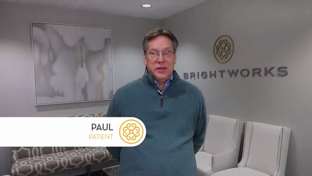 A man wearing glasses and a teal sweater stands in a modern waiting room with "Brightworks" signage on the wall behind him. Text overlay reads, "Paul, Patient.