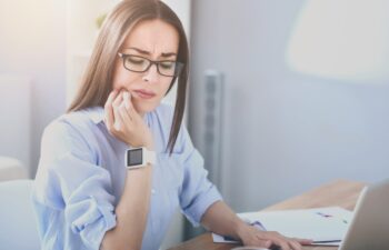 Unbearable toothache. Good looking bespectacled woman working on laptop and having toothache while sitting by the table.