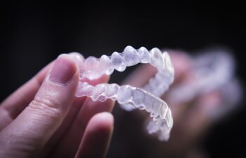 Woman hand holding invisible orthodontics. Black background.