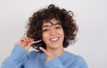 Young beautiful Arab woman holding an invisible aligner braces against white studio background and pointing at it. Dental healthcare concept.